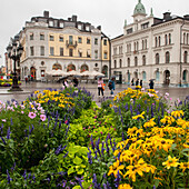 Pedestrians And Brightly Coloured Flowers In An Urban Area; Uppsala Sweden