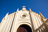 Niedriger Blickwinkel auf ein Kreuz über einem Kircheneingang vor blauem Himmel; Chiclana De La Frontera Andalusien Spai