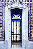 An Open Doorway On A Building With Ornate Facade Leading Into A Room With A Gate Surrounded By Blue Glass; Chiclana De La Frontera Andalusia Spain