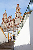 Ein Fußgänger geht die Stufen zu einem Gebäude mit zwei Türmen und einer Uhr hinauf; Olvera Andalusien Spanien