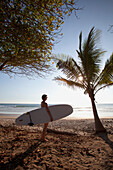 Eine Surferin hält ihr Surfbrett am Playa Santa Teresa (Santa Teresa Strand) in Santa Teresa und Mal Pais (Malpais) auf der Nicoya Halbinsel; Provinz Puntarenas, Costa Rica