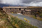 A Stone House On The Side Of A Road With Storm Clouds Overhead; Swaledale England