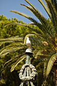 Ein Vogel sitzt auf einer Metallskulptur mit einer Palme im Hintergrund; Ventimiglia Italien