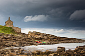 Red And Green Kayaks Sitting On The Rocky Shore With A House At The Water's Edge; Northumberland England