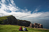 Zwei Menschen sitzen auf dem Gras und schauen durch ein Fernglas auf die felsige Landzunge bei St. Abb's Head; Scottish Borders Schottland