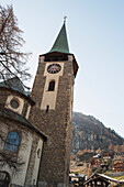 Uhrenturm und Kreuz einer Kirche mit Häusern auf dem Hügel im Hintergrund; Zermatt Wallis Schweiz