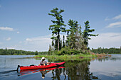 A Woman In A Red Kayak On A Tranquil Lake; Lake Of The Woods Ontario Canada