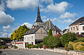 Eine Kirche und hängende Blumenkörbe an einer Steinmauer entlang einer Straße; Hergnies Ardennes Frankreich
