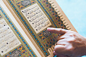A man reading from the koran with his finger pointing to the text; turkey