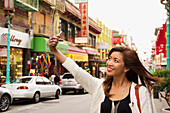 A woman takes a picture of herself with her cell phone camera in a busy urban area; san francisco california united states of america