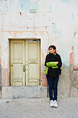 Frau steht neben einem kleinen, alten Eingangstor; San Luis de la Paz, Guanajuato, Mexiko