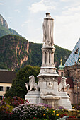 Italy, Alto Adige, Dolomites, Bolzano, Piazza Walther, Statue surrounded by flowers with cliffs in background
