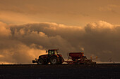 England, Northumberland, Traktor bei der Arbeit auf einem Feld unter einer Gewitterwolke