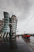 Czech Republic, Streetcar on wet road passes by building with curved architecture; Prague