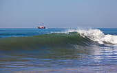 Mexico, Wave crashing close to shore with ship in distance; Puerto Vallarta