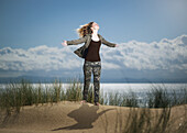 Spanien, Andalusien, Cadiz, Teenager-Mädchen, das mit ausgestreckten Armen auf einer Sanddüne steht und nach oben schaut; Tarifa