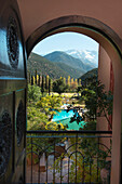 View Through An Arched Doorway To A Turquoise Pool Of Water And The Atlas Mountains In The Background; Marrakech-Tensift-El Haouz, Morocco