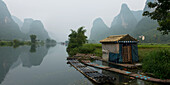 Ein kleines Gebäude und Boote entlang des Ufers des Yulong Flusses; Guilin, Guangxi, China