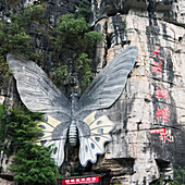 Ein großer Schmetterling an einem Berghang über einem Schild; Guilin, Guangxi, China