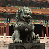 Eine Löwenstatue vor einem Gebäude mit bunter, verzierter Fassade in der Verbotenen Stadt; Peking, China