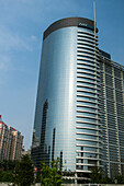 Ein Wolkenkratzer mit einer abgerundeten Seite, in der sich andere Gebäude in der Glaswand spiegeln; Peking, China