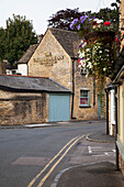 Eine Straße mit Blumenkörben, die an der Seite eines Gebäudes hängen, und das Kingsbridge Inn; England