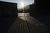 Sonnenlicht, das durch ein Metalltor mit einem Kreuz darauf scheint; Bellinzona, Tessin, Schweiz