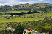 Ein Bus fährt eine landschaftlich reizvolle Straße entlang, gleich außerhalb von Hyde in der neuseeländischen Region Otago; Neuseeland
