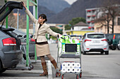 Eine Frau belädt ihr Auto mit Einkaufstüten auf einem Parkplatz; Ascona, Tessin, Schweiz
