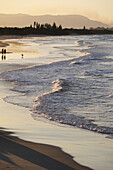 Silhouette von Menschen, die am Strand spazieren gehen, während pastellfarbene Wellen an die Küste schlagen, in Byron Bay in New South Wales, Australien