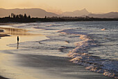 Silhouette einer Person am Strand, die den Wellen beim Auftreffen auf den Strand in Byron Bay in New South Wales, Australien, zusieht