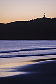 Silhouette des Cape Byron Leuchtturms auf der Bergspitze und am Strand bei Sonnenuntergang in Byron Bay in New South Wales, Australien