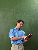 Teacher with Book in Front of Blackboard