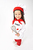Kleines Mädchen als Koch verkleidet hält einen Schneebesen