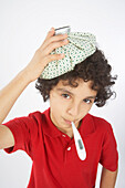 Junge mit einem Thermometer im Mund und einem Eisbeutel auf dem Kopf