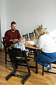 Eltern mit Kleinkind mit Down-Syndrom sitzen am Tisch