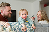 Parents playing with smiling baby Parents with baby with down syndrome reading a book on sofa on sofa in living room