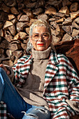 Porträt einer modischen Seniorin mit coolem Haarschnitt, die sich neben einem Brennholzstapel entspannt