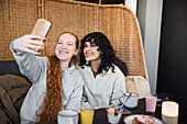 Smiling young women taking selfie in cafe
