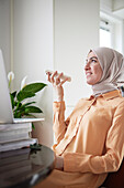 Lächelnde Frau mit Hidschab unterhält sich mit einem Kollegen oder Freund über den Lautsprecher