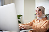 Lächelnde Frau mit Hidschab am Laptop