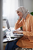 Smiling woman with hijab working from home using laptop
