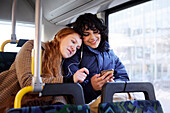 Freundinnen sitzen zusammen im Bus und schauen auf ihr Handy