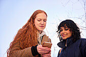 Freundinnen schauen auf ein Handy im Freien mit Sonne im Hintergrund