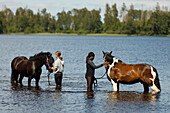 Girls with horses standing in river