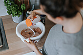 Woman putting salt over meat in bowl