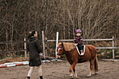 Girl horseback riding with female instructor on paddock
