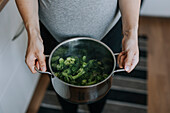 Woman's hands holding saucepan with boiled broccoli