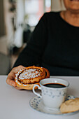 Hand hält Zimtschnecke, im Vordergrund Kaffee