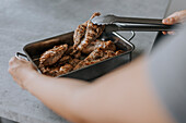 Hand holding tongs over container with grilled meat